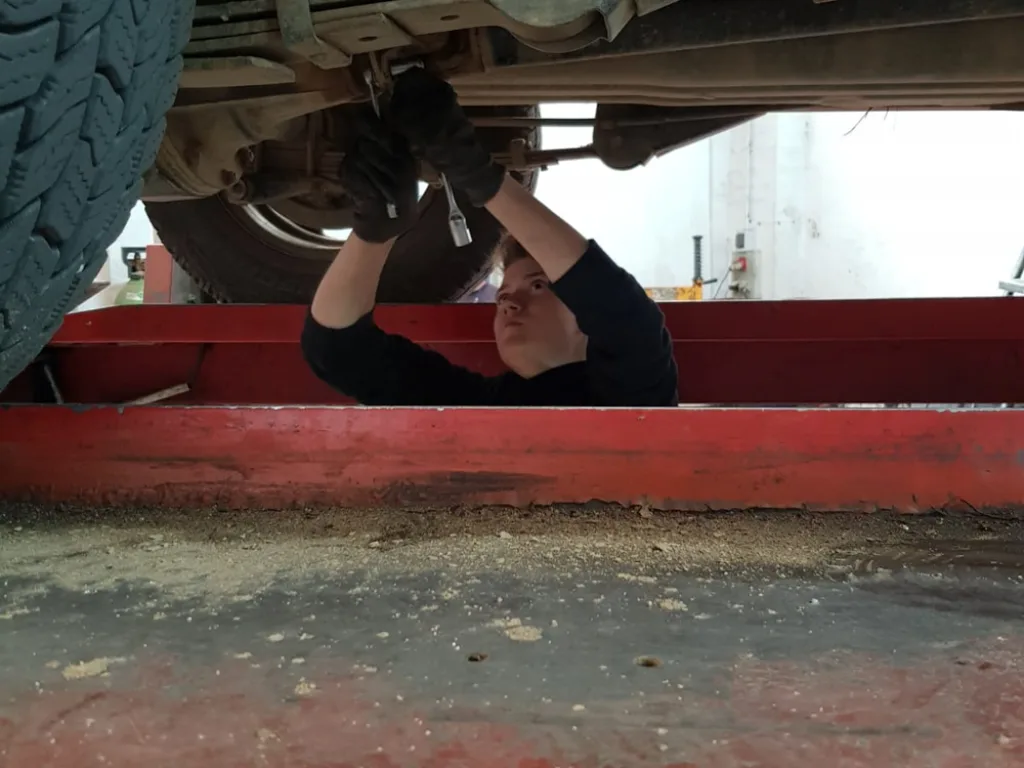Eine Person arbeitet unter einem aufgebockten Traktor.